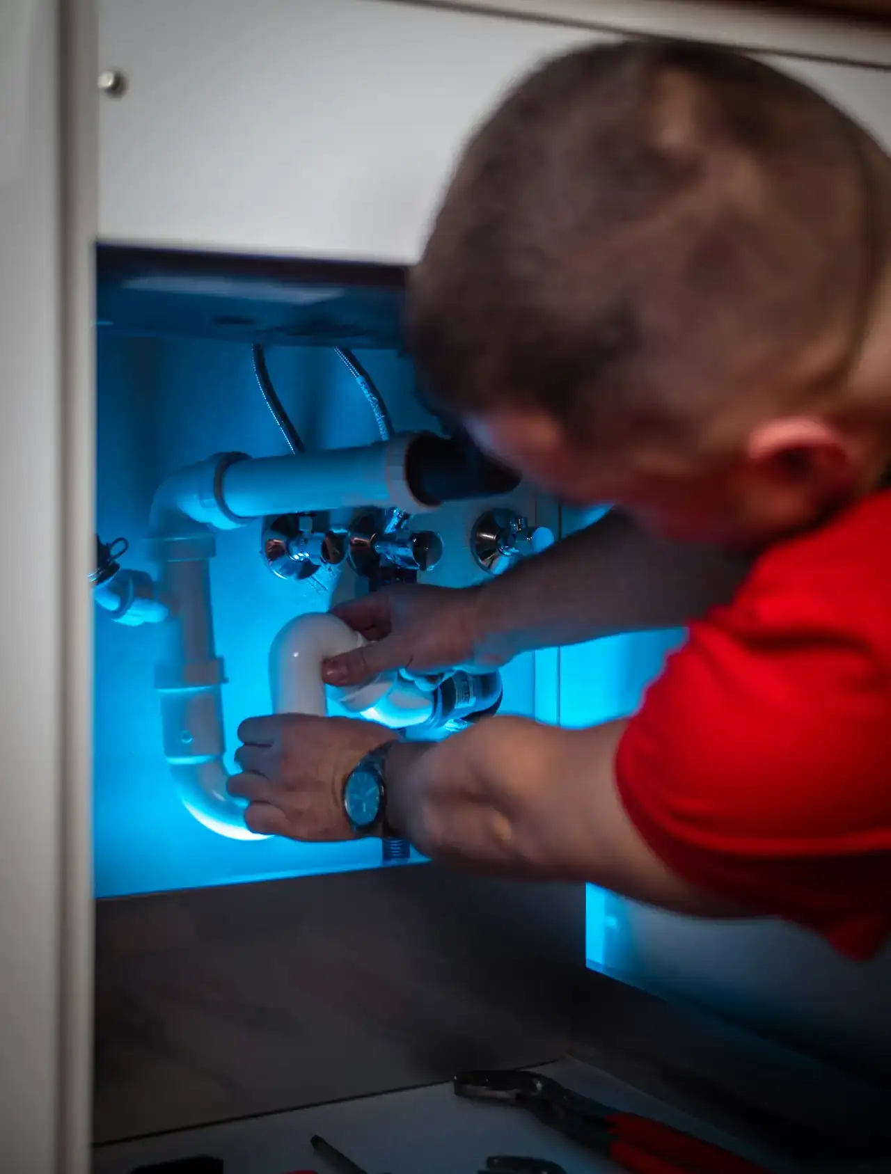 Plumber working on pipes inside a kitchen cabinet