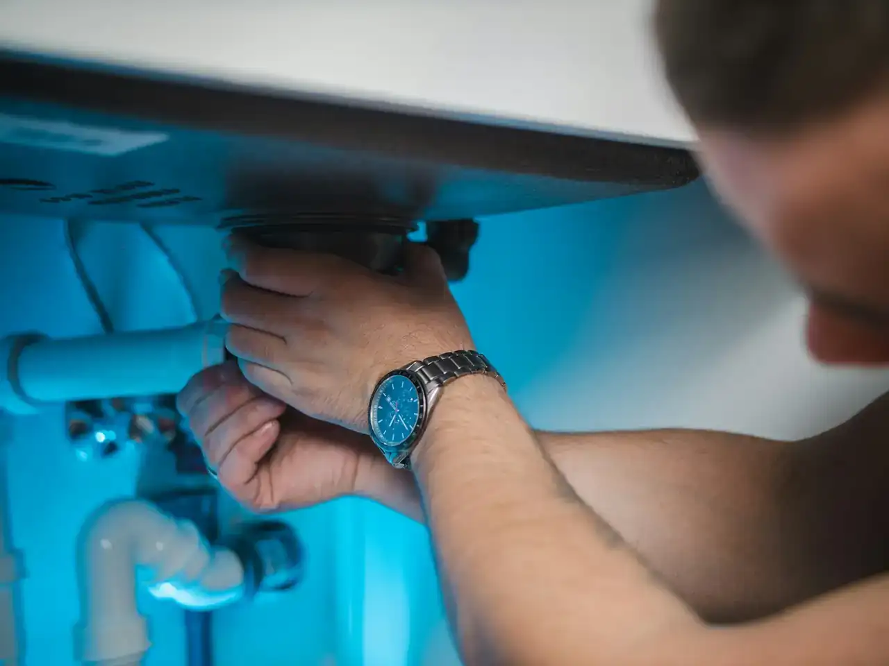 Plumber tightening a drain fitting under a sink